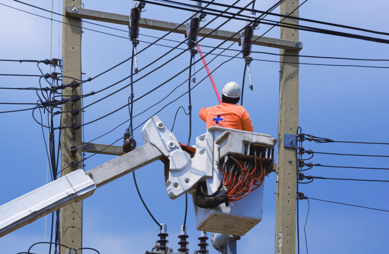 Low angle view of electrician with disconnect stick tool on crane truck are working to install electrical transmission on power pole against blue sky